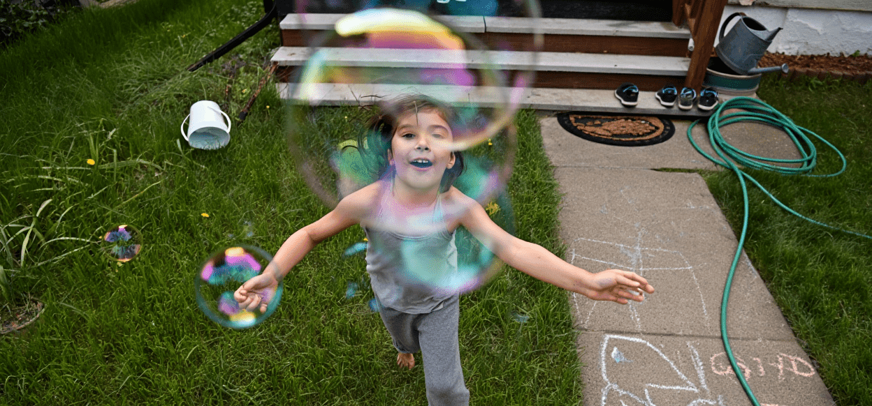 Smiling child playing with colorful bubbles in a green yard.