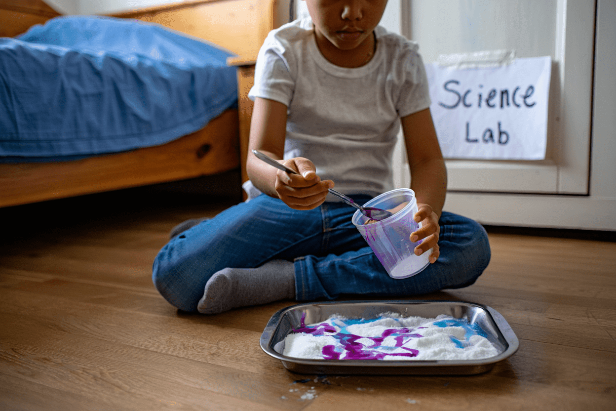 Child mixing purple liquid into white powder on a tray.